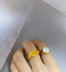 Close-up of a gold signet ring paired with a white shell inlay ring on a hand