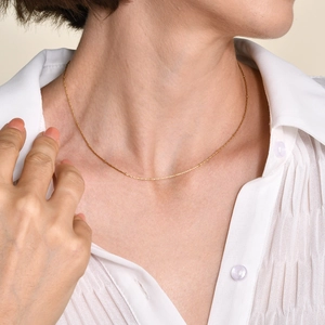 Détail d'un collier chaîne de 1 mm en acier doré avec perles sur le cou d'une femme
