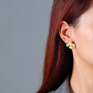 Detail of golden flower stud earrings with three pearls worn by a female model