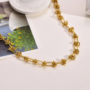 Détail du collier à nœuds dorés sur fond blanc avec un décor floral artistique