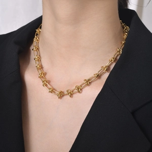 Collier à maillons noués en acier titane doré porté sur une veste de costume noire chic