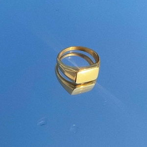 Polished gold square signet ring with white shell inlay on a blue reflective surface