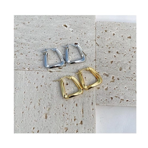 Macro detail of gold and silver chunky square hoop earrings on a beige travertine stone
