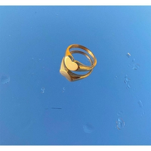Polished gold heart signet ring on a reflective blue surface with water droplets
