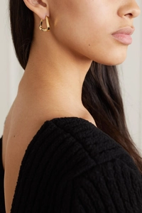 Close-up of golden twisted geometric stud earrings worn on ear with metallic luster