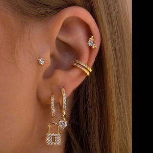 Close-up of gold ear jewelry set with heart and lock charms featuring sparkling zircon stones