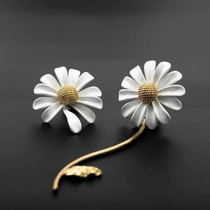 Detail of white daisy earrings with golden stems and leaves on a black background
