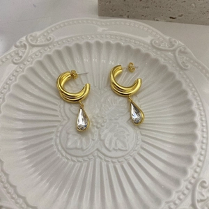 Detail of gold-plated double-hoop earrings with pear-shaped crystal drops on white tray