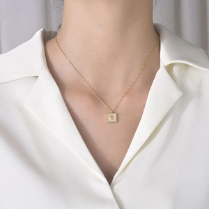 Gros plan d'un collier pendentif rose carrée dorée porté par un mannequin chic