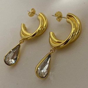 Detail of gold twisted C-shape brass earrings featuring teardrop crystal pendants