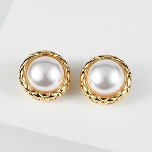 Detailed view of gold round earrings with white pearl inlay and diamond pattern texture