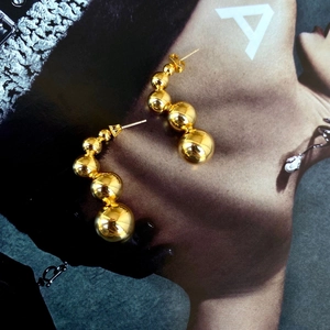 Detail of gold beaded drop earrings with mirror polished finish on a fashion magazine
