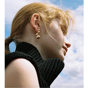 Macro close-up of a model wearing tiered gold spherical earrings against a blue sky