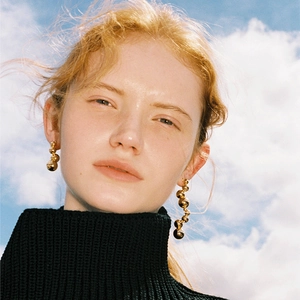Detail of long drop gold ball earrings worn by model against a blue sky background
