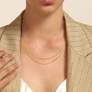 Détail d'un collier double rang doré porté sur un blazer marron élégant et chic