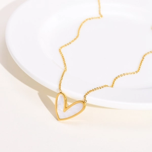 Collier cœur doré minimaliste avec incrustation en nacre sur une assiette en porcelaine