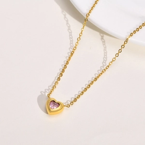 Detailed close-up of a gold heart pendant necklace featuring a sparkling pink gemstone