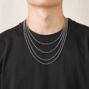 Detail showing various lengths of 3mm Figaro chain necklaces layered on a black t-shirt