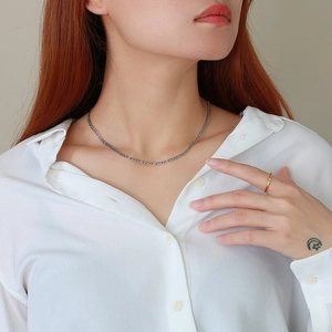 Macro shot of 3mm silver Figaro chain necklace and gold ring on a female model