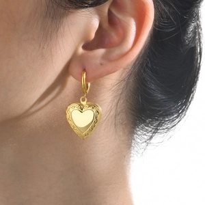 Elegant gold heart earrings with vintage scroll patterns worn by a model in a close-up view
