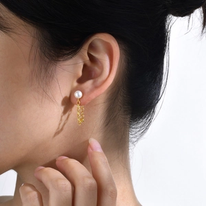 Dettaglio di un orecchino con perla e catena d'oro indossato da una modella in luce naturale