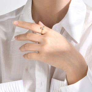 Detailed view of a gold twisted band ring with a square white zircon on a model's finger
