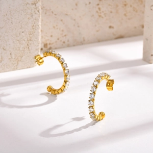 Detail von goldenen C-förmigen Titanstahlohrringen mit Zirkonia-Besatz auf Steinuntergrund