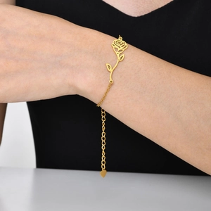 Detail view of a rose charm bracelet in gold finish worn on wrist with adjustable heart clasp