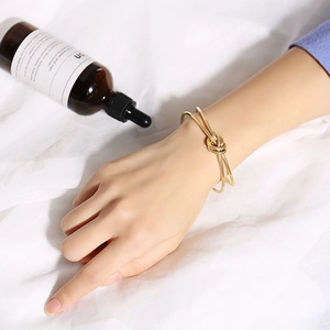 Dettaglio di un bracciale rigido a nodo dorato sul polso con sfondo minimalista
