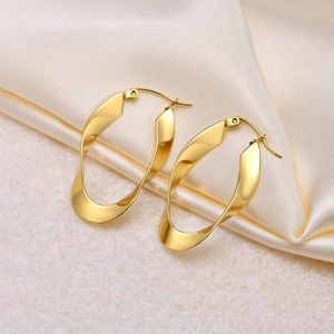Polished gold Mobius twist hoop earrings on a marble surface with elegant silk backdrop