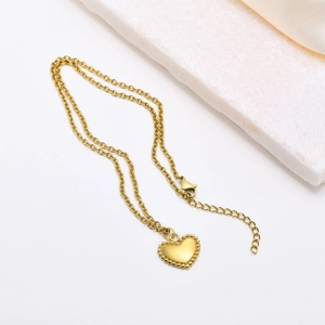 Golden stainless steel heart pendant necklace with beaded edges and O-chain on marble