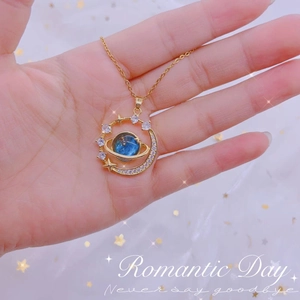 Detailopname van een gouden ketting met blauwe planeet en zirkoon maan hanger