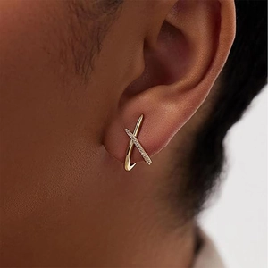 Close-up of gold X-shaped cross earrings with pavé crystals worn by a model