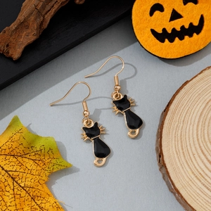 Détail de boucles d'oreilles chat en émail noir avec contours dorés sur fond d'automne