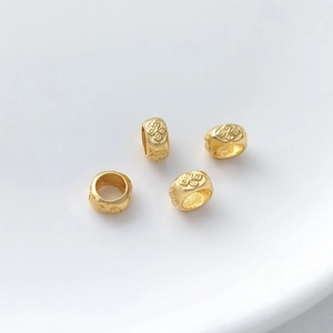 Detail view of four matte gold cylinder beads with embossed floral patterns for jewelry