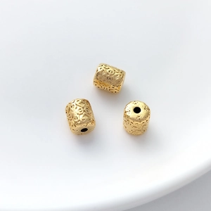 Macro shot of three gold barrel beads with detailed floral relief for DIY jewelry making