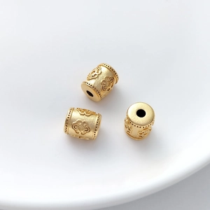 Macro shot of three gold flower embossed cylinder beads on a white ceramic plate
