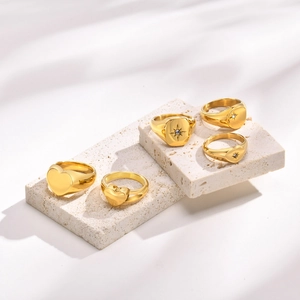 Detail of five gold minimalist signet rings with heart and star patterns on stone props