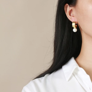 Close-up of elegant gold wide C-hoop earring with hanging white round pearl on a model