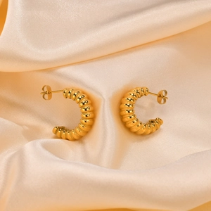 Polished gold C-shaped hoop earrings with textured stripes on champagne silk fabric