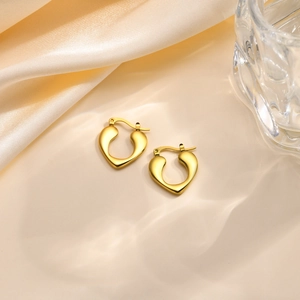Nahaufnahme goldener herzförmiger Creolen auf elegantem Seiden- und Glashintergrund