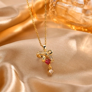 Vista macro de un collar de lazo dorado con circonita de corazón rojo y pequeños cristales