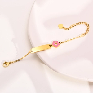 Detail of gold ID bracelet with pink enamel flower and heart charm on white ceramic