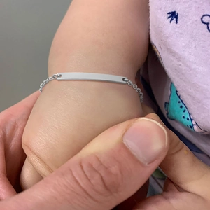 Detailed macro view of a baby's wrist wearing a polished stainless steel ID tag bracelet