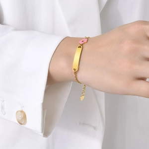 Close-up of golden bar bracelet with a pink enamel flower and heart charm on wrist