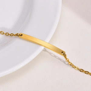 Close-up of polished gold-tone stainless steel ID bar bracelet on a white ceramic plate
