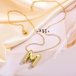 Macro detail of golden bubble letter M pendant with lobster clasp and O-chain texture
