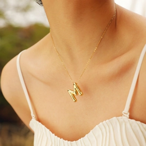 Close-up of golden balloon-style M letter pendant on a delicate chain worn by a model