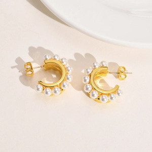 Détail de boucles d'oreilles créoles dorées en C avec perles blanches sur fond beige