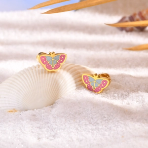 Gouden vlinder oorknopjes met roze en blauw emaille op schelpen en wit zand